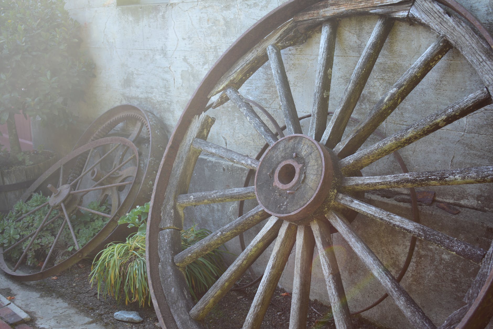 Several old wooden wagon wheels leaning against a concrete wall.